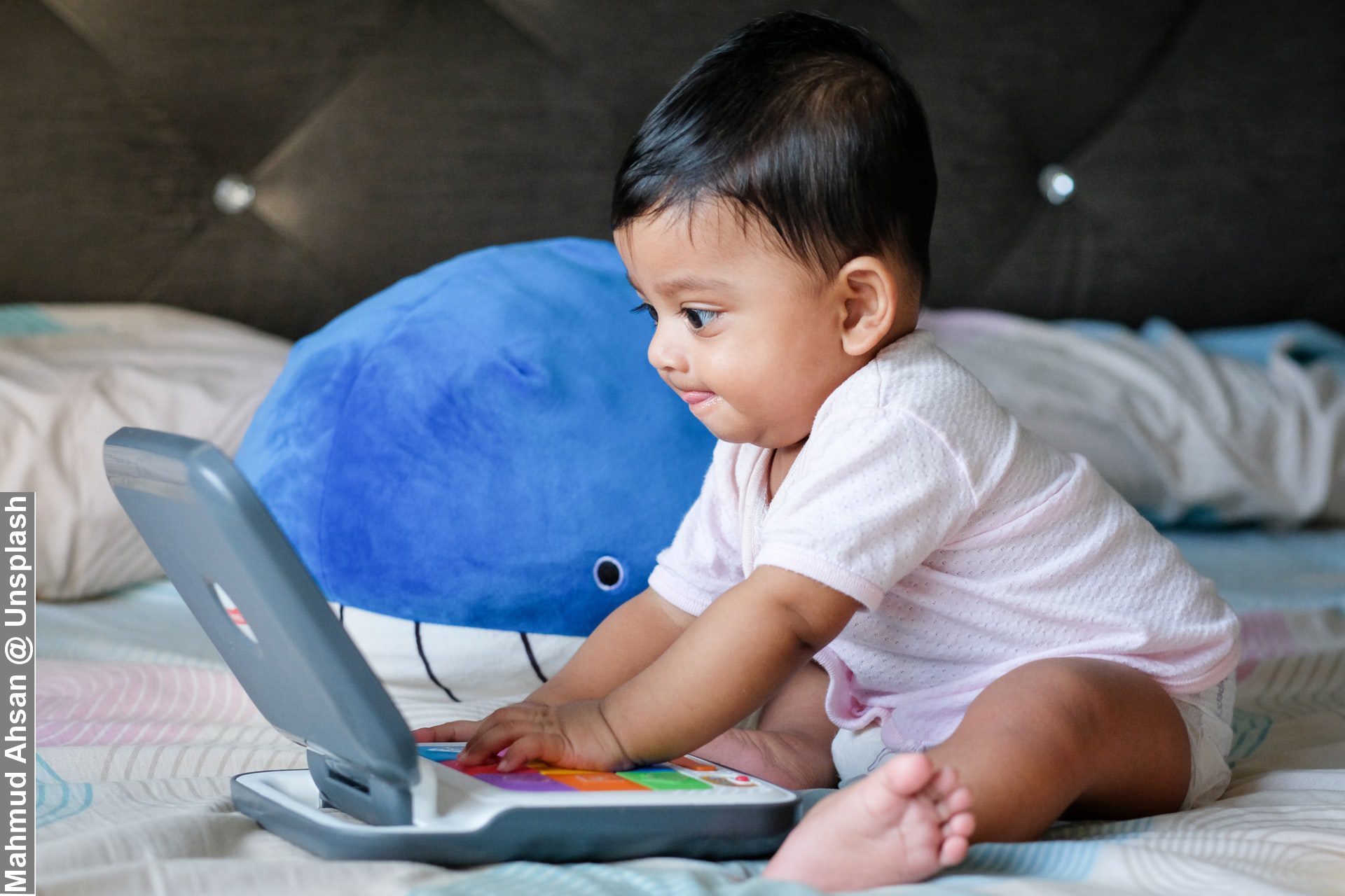 Baby engaged in his unique working routines on bed with baby laptop