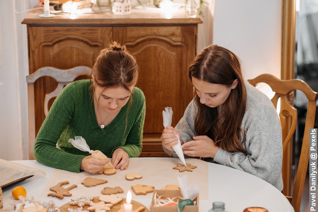 Late Christmas decorations, two young women putting icing on Christmas cookies