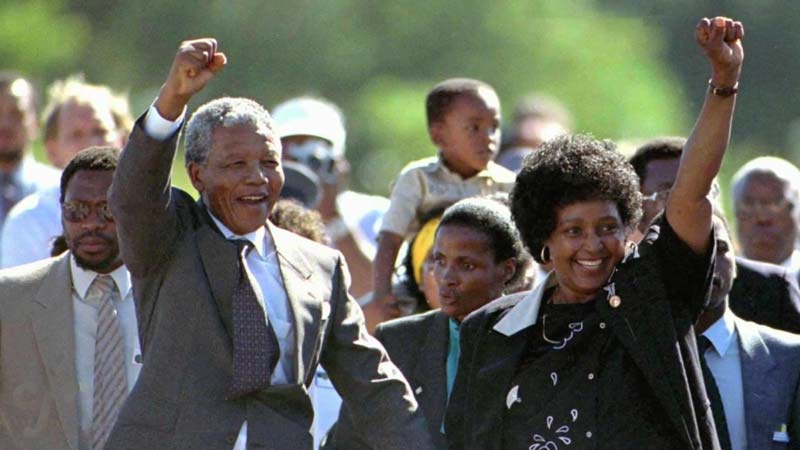 Nelson Mandela and Winnie Mandela raising their fists in triumph as they walk together surrounded by supporters.